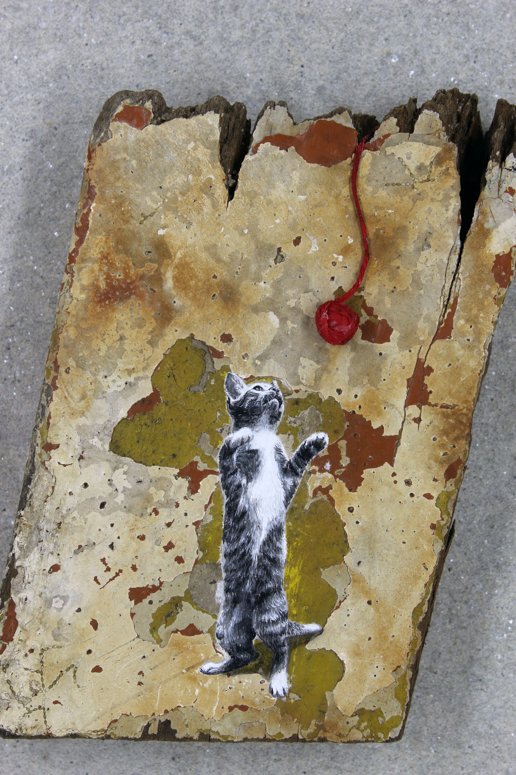 Small rectangular piece of stone with a painted cat and red ball of string on a gray background