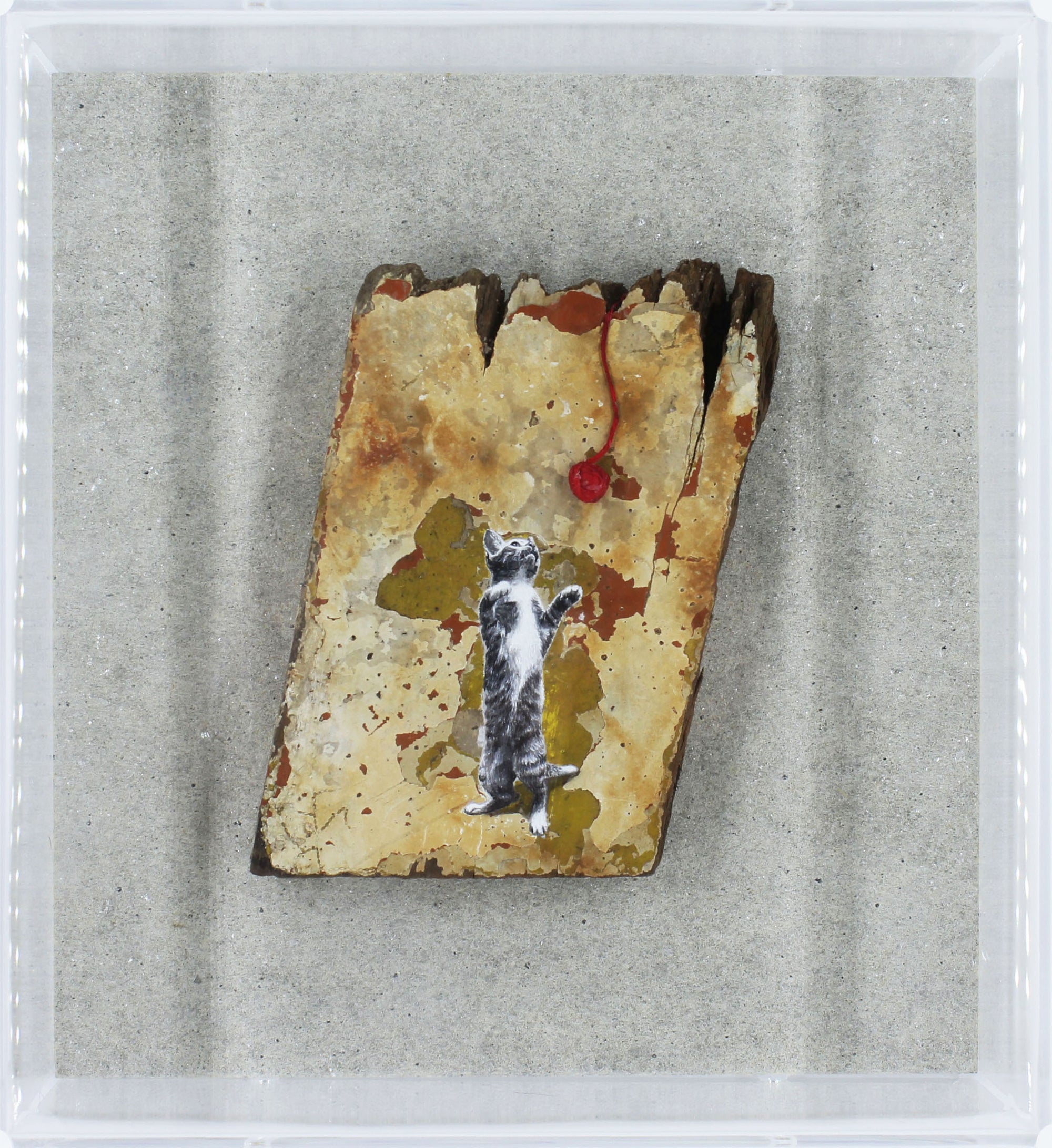 Small rectangular piece of stone with a painted cat and red ball of string on a gray background