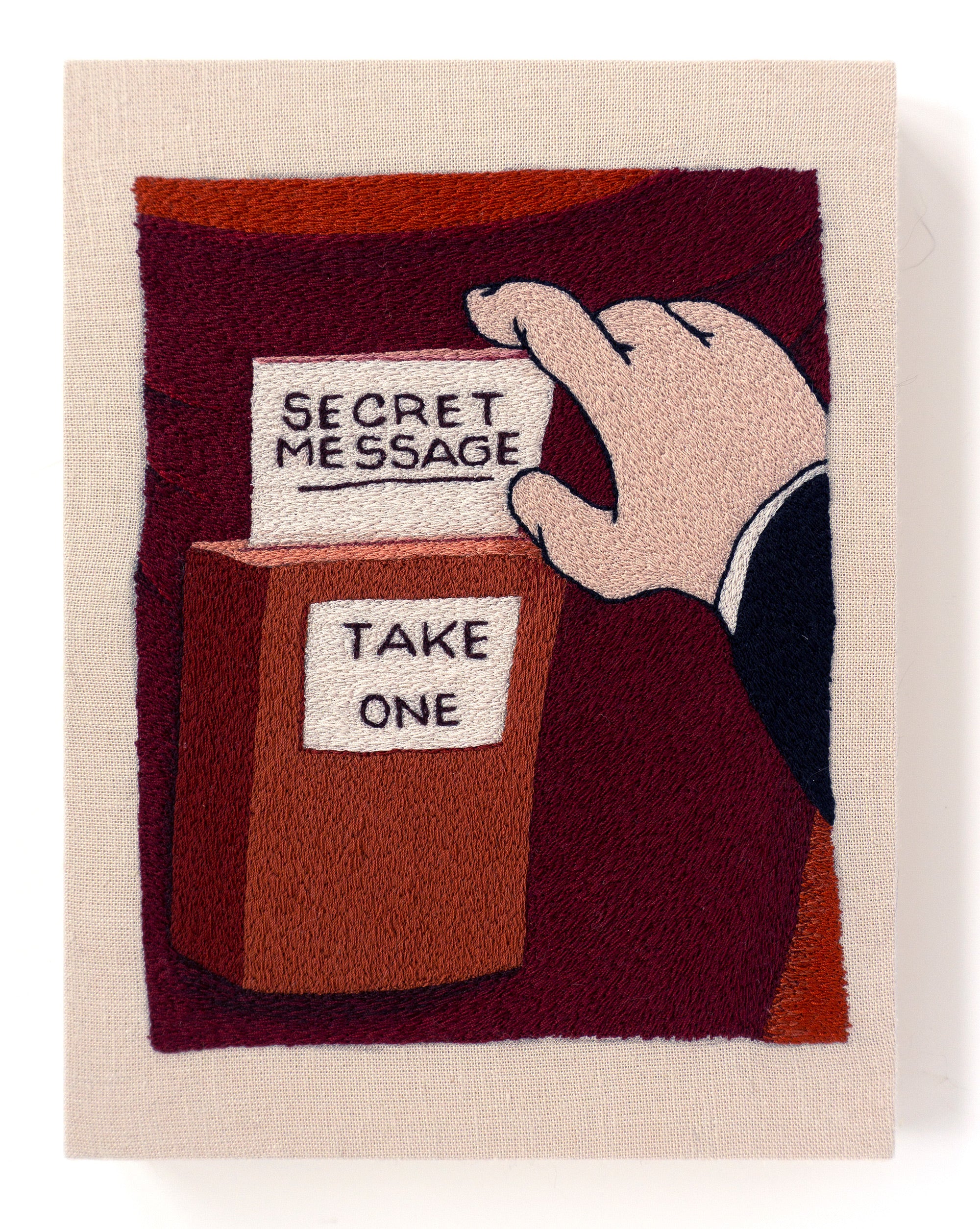 an embroidery of a hand taking a secret message from a box that says take one